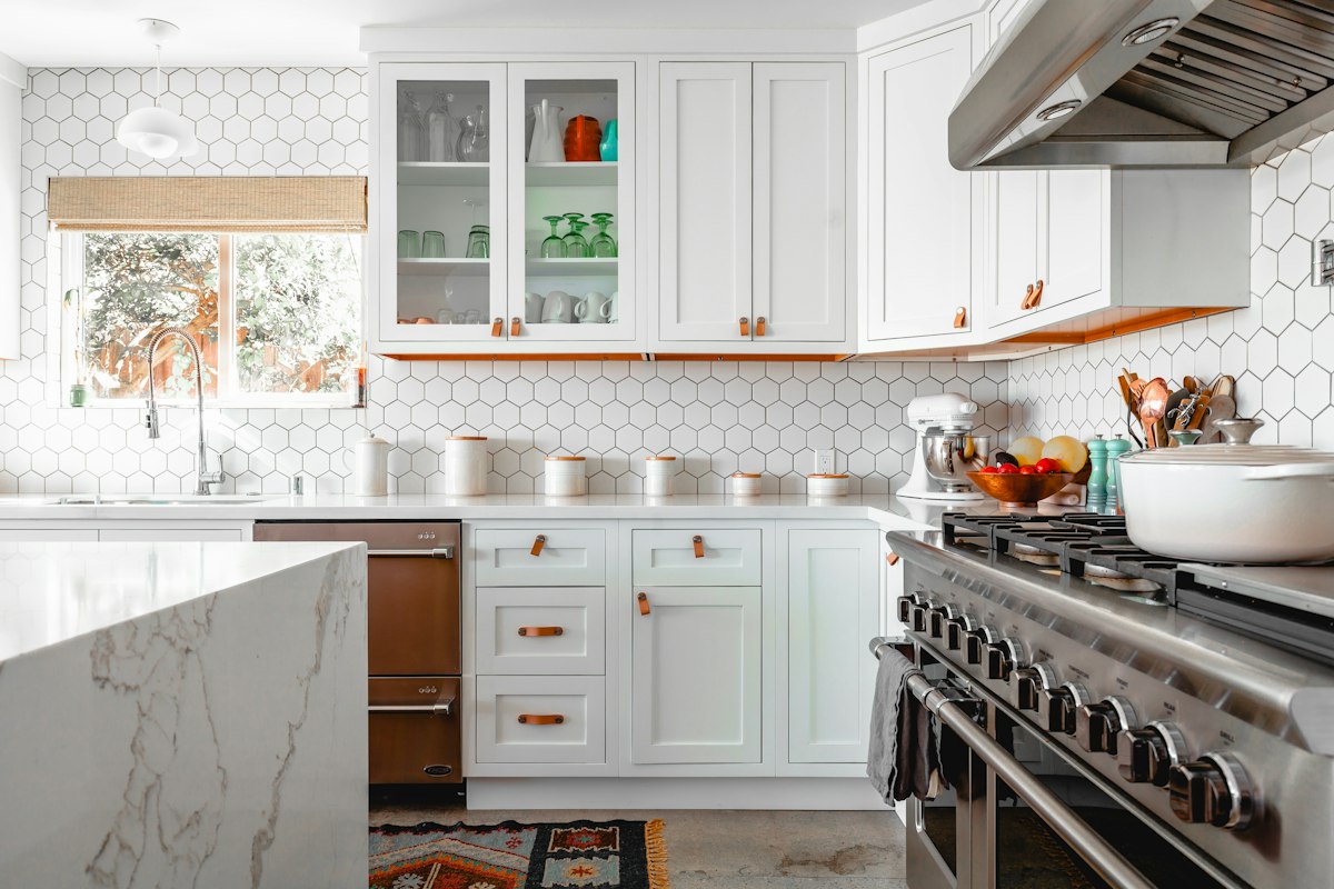 Renovated kitchen with white shaker cabinetry, marble island and patterned tile splashback