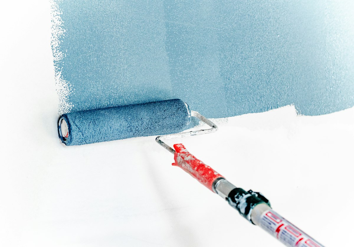 Paint roller applying a calm blue paint to a prepared wall